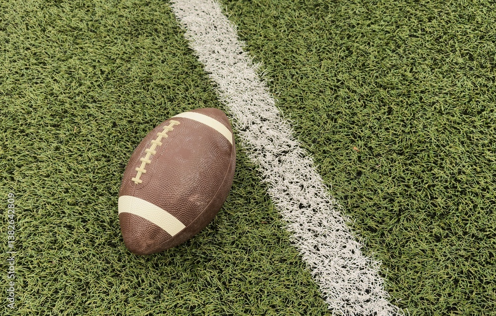 Fototapeta premium Leather american football ball on grass of football field at stadium. Concept of sport, art, energy, power. Poster for ad, design
