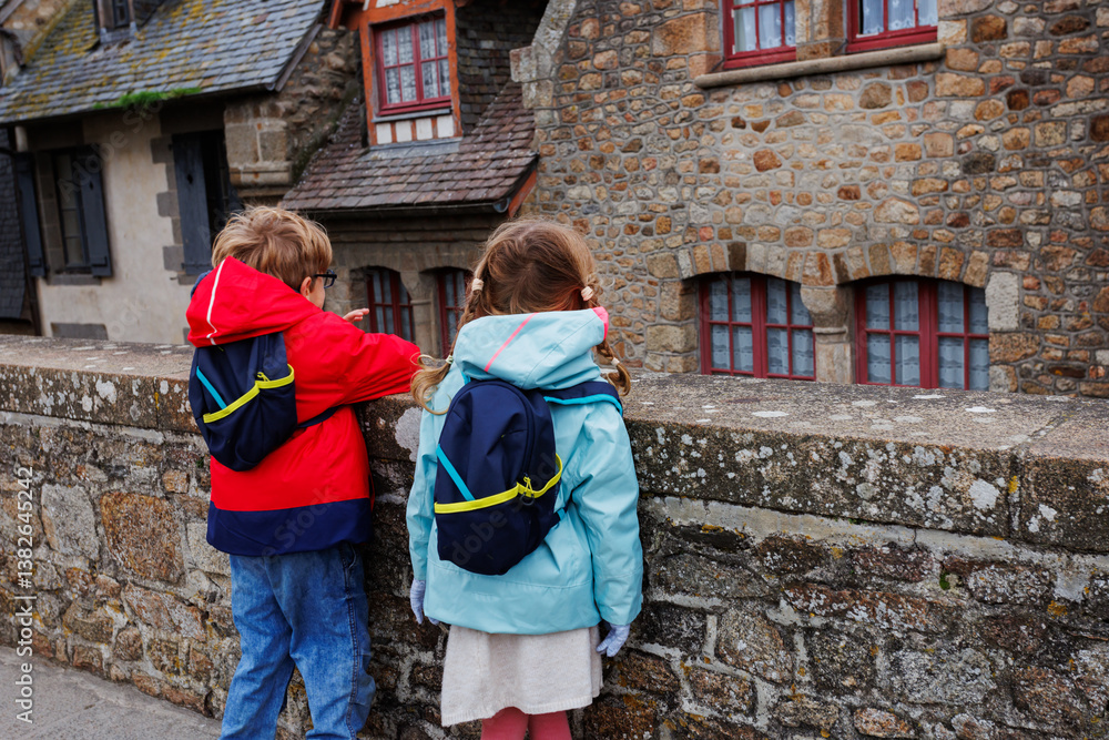 Curious kids in jackets and backpacks observe stone architecture