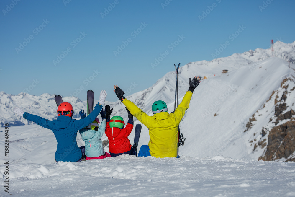 Skiing family in vibrant outfits sits together on snowy peak