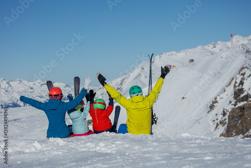 Skiing family in vibrant outfits sits together on snowy peak
