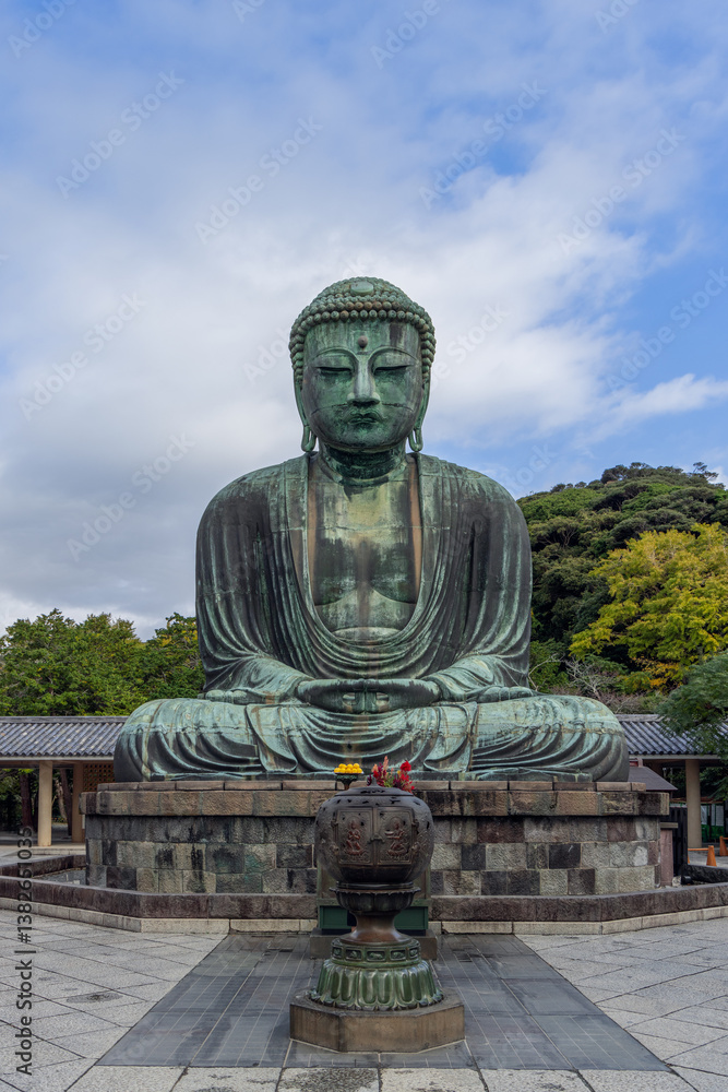 Majestic bronze Buddha seated in meditation at Kotoku-in temple with ritual offerings placed before it framed by greenery temple structures Majestic bronze Buddha seated in meditation at Kotoku-in temple with ritual offerings placed before it framed by greenery temple structures