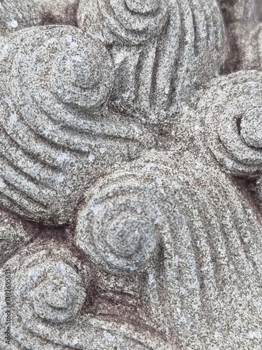 a close-up of a stone carving with a spiral pattern. The carving is made of gray stone and has a rough, textured surface