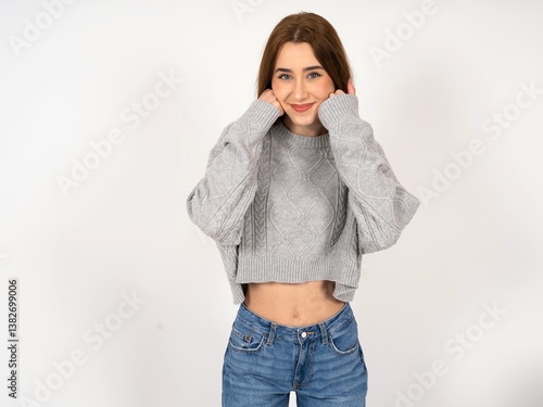 Happy Caucasian young girl wearing grey sweater keeps fists on cheeks smiles broadly and has positive expression being in good mood