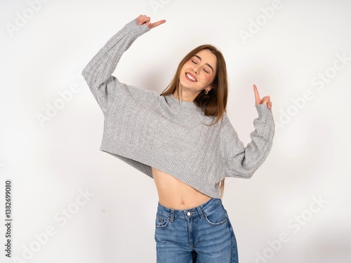 Photo of upbeat Caucasian young girl wearing grey sweater has fun and dances carefree wear being in perfect mood makes movements. Spends free time on disco party