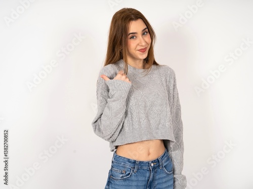 Caucasian young girl wearing grey sweater points away and gives advice demonstrates advertisement