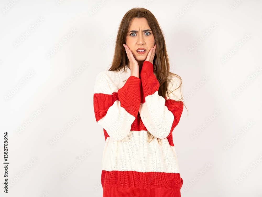 Fototapeta premium Upset Caucasian young girl wearing striped sweater touching face with two hands