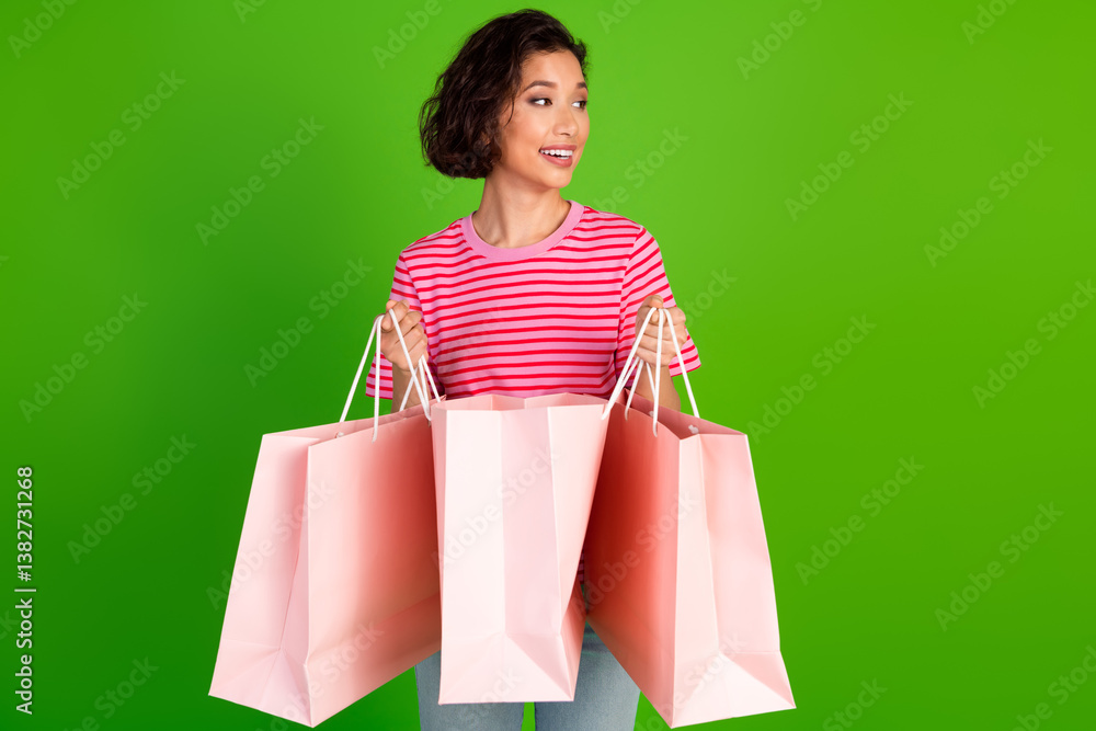 Young woman holding pink shopping bags smiling cheerfully against a bright green background al wear Young woman holding pink shopping bags smiling cheerfully against a bright green background al wear