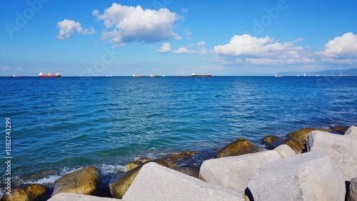 Peaceful seaside view with clear blue waters, rocky coast and a few boats in the distance.