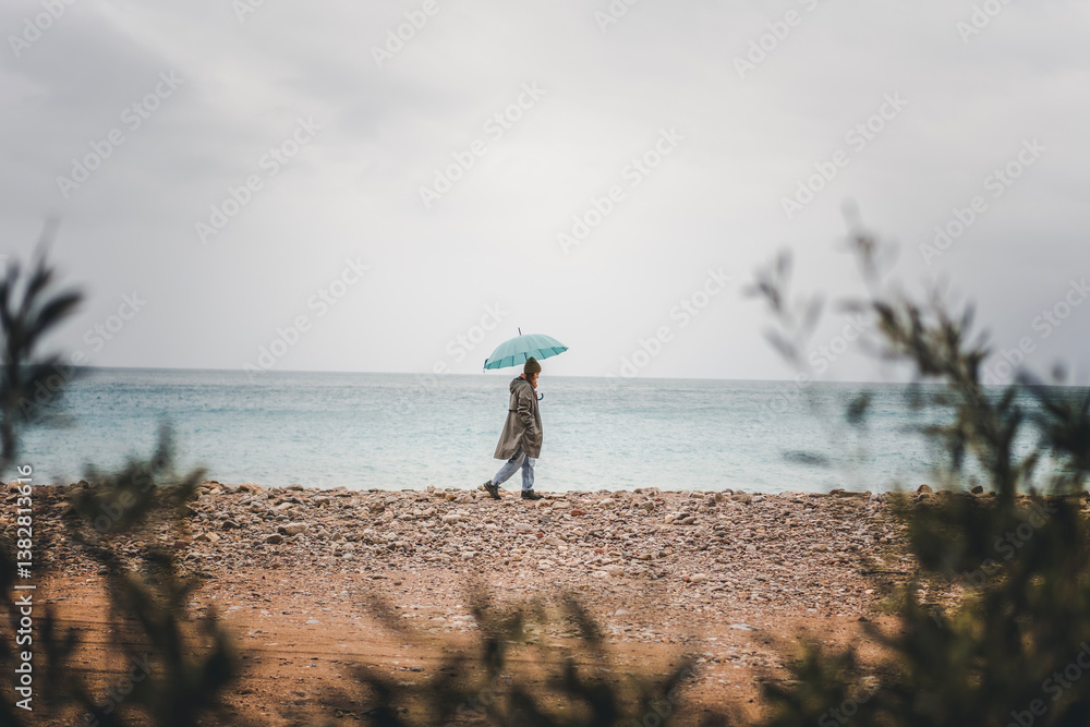 Young woman walking in the rain with a blue umbrella on the seashore