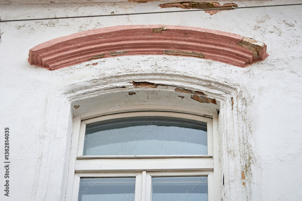 Vintage window with visible wear, reflecting intricate details of historic craftsmanship. Old window with curved red painted arch above. Weathered window frame and arch. Frame is chipped and peeling