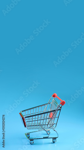 a miniature shopping cart against a plain vertical blue background