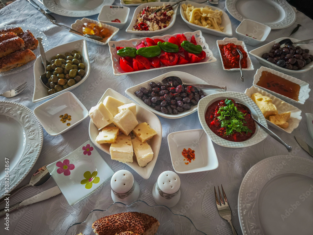 Turkish breakfast table. Flat-lay of peoples hands taking pastries, vegetables, greens, olives, cheeses, fried eggs, spices, jams, honey, tea in copper pot and tulip glasses, wide composition