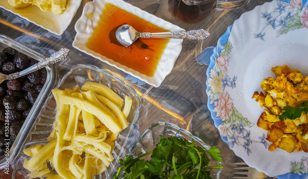 Turkish breakfast table. Flat-lay of peoples hands taking pastries, vegetables, greens, olives, cheeses, fried eggs, spices, jams, honey, tea in copper pot and tulip glasses, wide composition