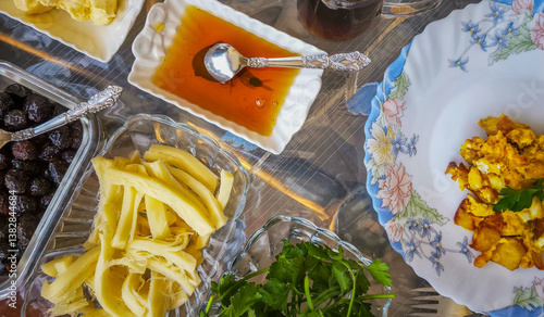 Turkish breakfast table. Flat-lay of peoples hands taking pastries, vegetables, greens, olives, cheeses, fried eggs, spices, jams, honey, tea in copper pot and tulip glasses, wide composition