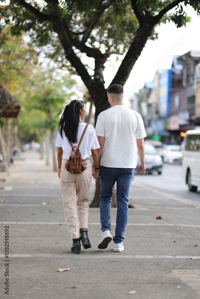 Two young tourists happily walk hand in hand in a tourist area in a city in Thailand. Two young tourists happily walk hand in hand in a tourist area in a city in Thailand.