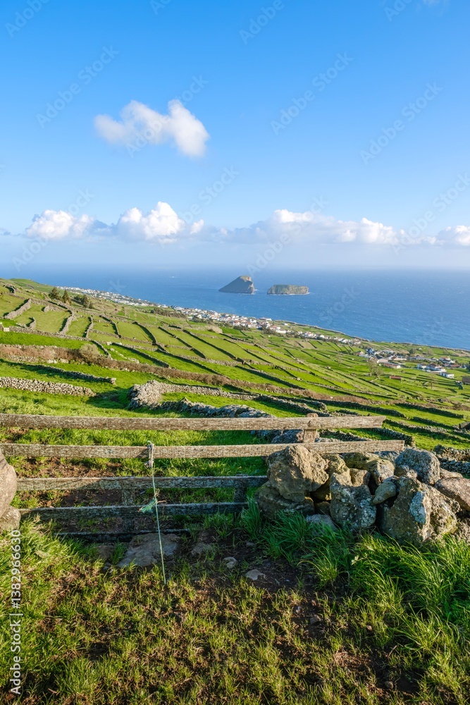 A stunning panoramic view of Terceira, Azores, showcases the island unique rural landscape with its green fields, stone walls, wood fence, and a picturesque coastal vista