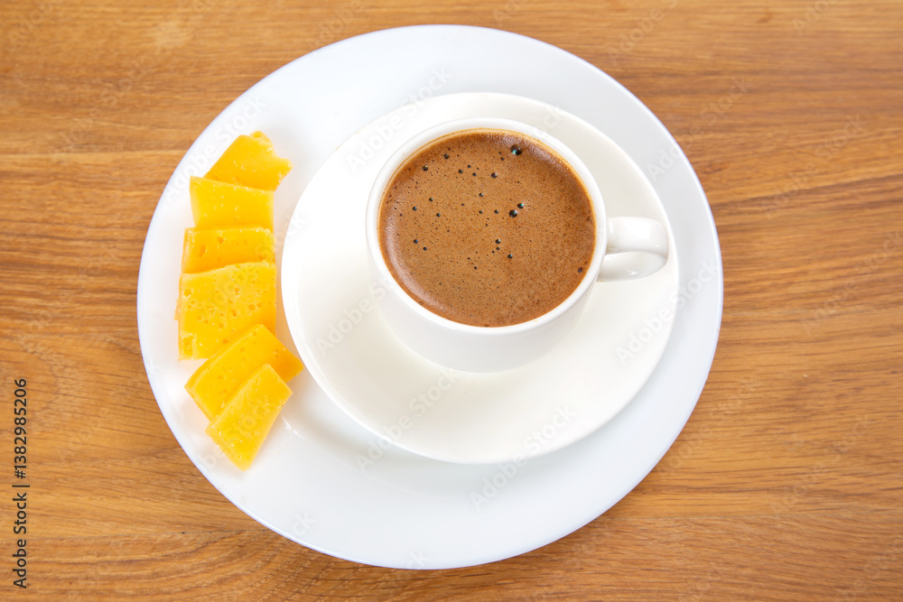 Obraz premium top-down view of a white cup of espresso with a frothy surface on a saucer, paired with slices of yellow cheese on a wooden table. Minimalistic and rustic setting.