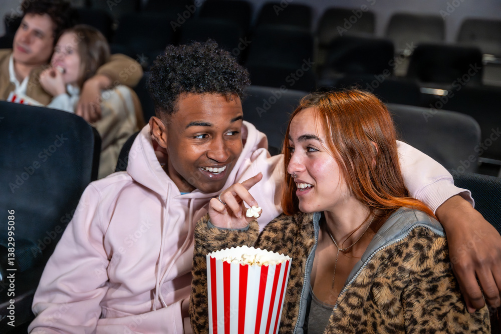 Young couple sharing popcorn and whispering in movie theater
