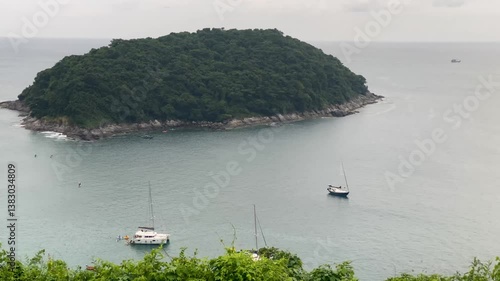 Aerial view of a green cape on Phuket Island, Thailand, with anchored sailboats, a small beach, and a distant island under golden light-4k