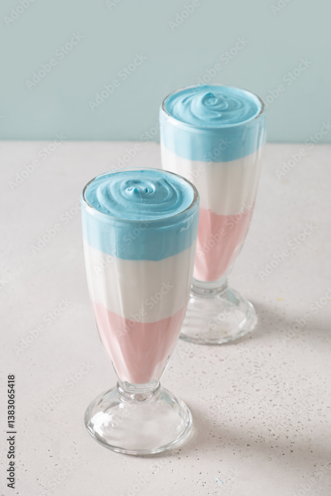 Two Patriotic layered milkshake, cocktail or sweet dessert for child for Independence Day on blue background. Vertical. Food for 4th of July or Memorial Day.