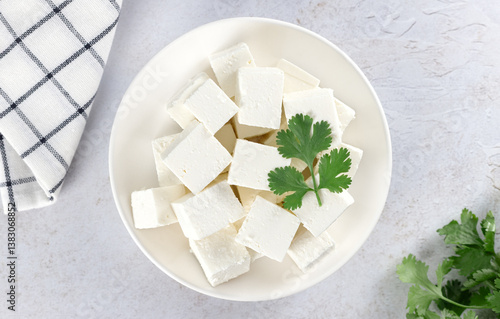 Cubes of traditional Indian paneer cheese made from fresh milk and lemon with cilantro on white background. Top view.