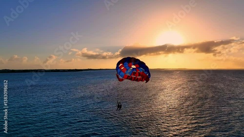 Two people parasailing over the sea waters at sunset, capturing the colors of a Caribbean evening