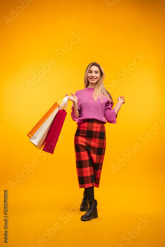 Smiling woman dressed in stylish plaid and vibrant colors, holding shopping bags with cheerful energy on a striking yellow background, representing shopping, joy, fashion, and colorful trends.