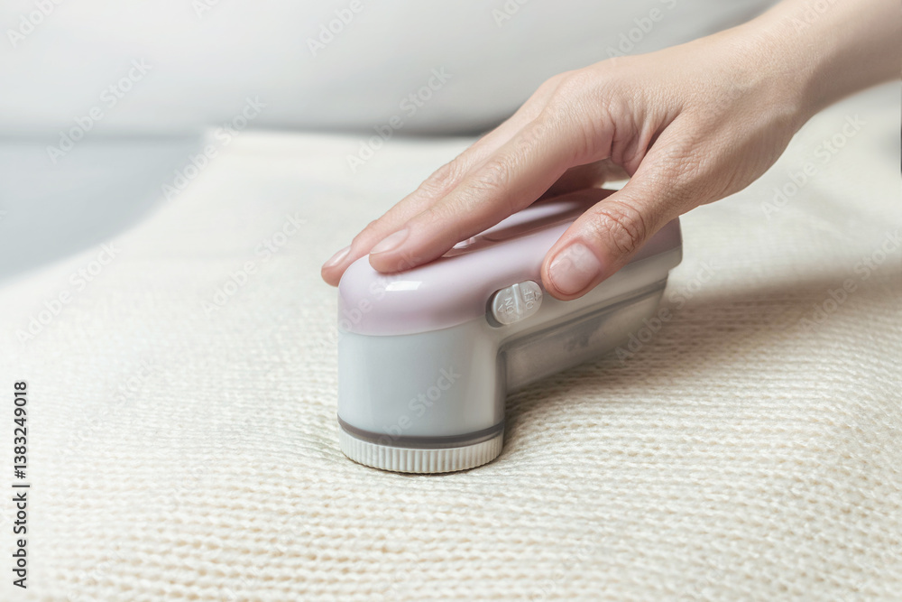 Fototapeta premium Machine for removing pellets from a woolen white jacket. A hand holds a reel removal machine close up photo