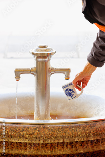 Patient füllt Porzellanbecher an einer heißen Thermalquelle im europäischen Kurort Karlovy Vary mit heilendem Wasser auf - Karlsbad, Tschechien 2025-03-27