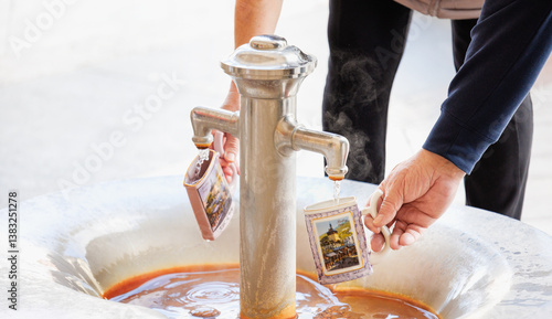 Zwei Personen Rentner füllen heißes Heilwasser aus einem Thermalbrunnen in traditionell verzierte Kurbecher in einem historischen Kurort Karlovy Vary - Karlsbad, Tschechien 2025-03-27