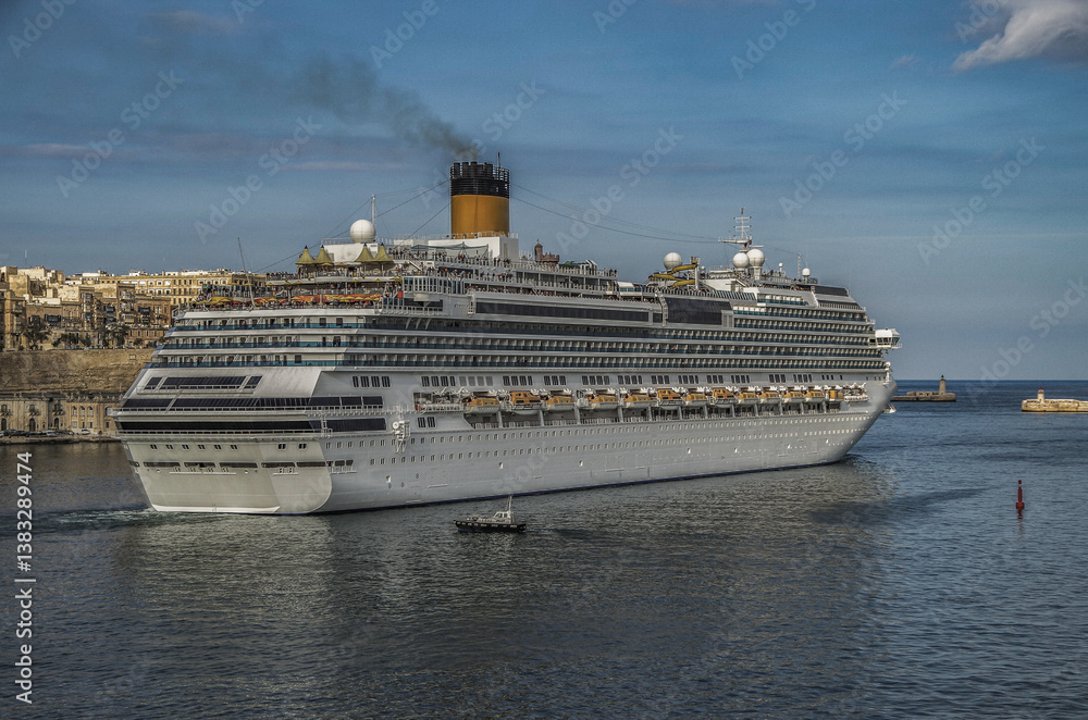 Gigantic cruiseship cruise ship liner Fascinosa docked at pier terminal in old town Valletta, Malta with historic buildings, city skyline and harbor entrance