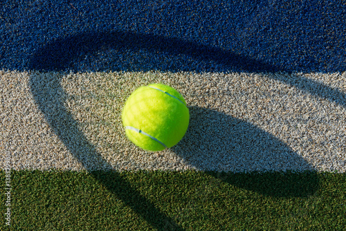 Close-up of Tennis Ball on blue/green synthetic court with shadow of tennis racket