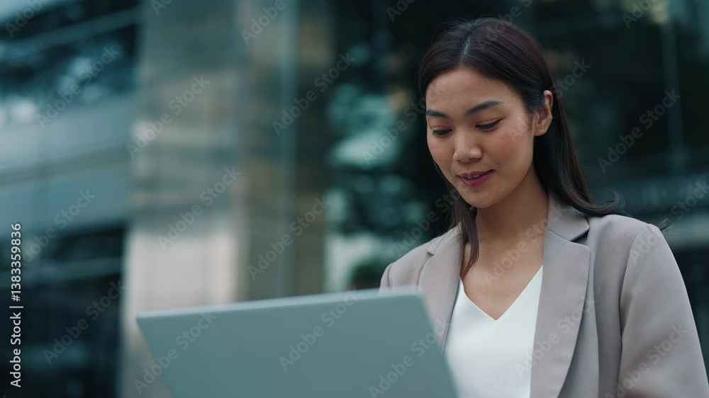 Portrait of Thai woman working on laptop sitting near office building