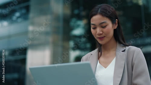 Portrait of Thai woman working on laptop sitting near office building