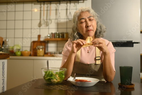 Papier peint A Senior Asian Woman Savoring a Homemade Sandwich in Cozy Kitchen Setting