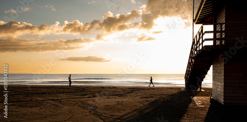 Tourists walking on the beach at sunrise near a lifeguard tower at sunrice