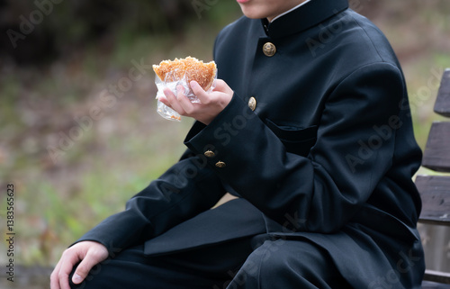 ベンチに座ってパンを食べる男子学生