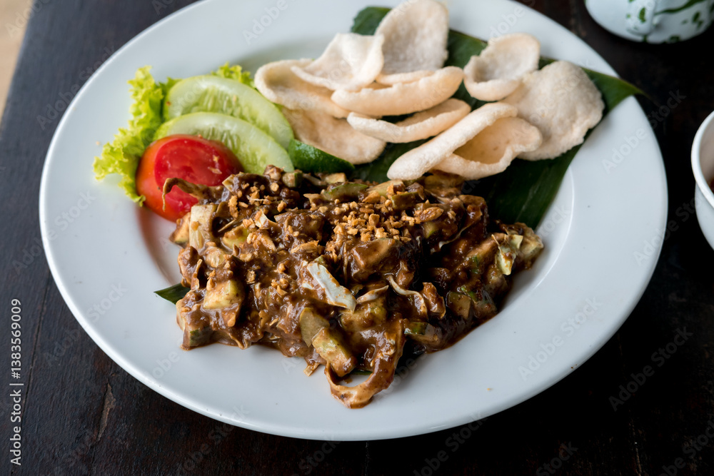 Lotek, a Sundanese vegetable salad with peanut sauce, served with crackers, lime, cucumber, and tomato on a white plate. Rich and flavorful Indonesian dish. Lotek, a Sundanese vegetable salad with peanut sauce, served with crackers, lime, cucumber, and tomato on a white plate. Rich and flavorful Indonesian dish.