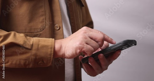 Man in brown shirt holding smartphone in his hand and typing on it. Concept of work anywhere, online communication technology and mobile worker.