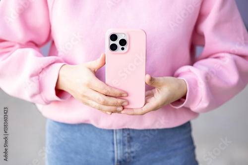 Woman holding phone in pink protective case pink sweatshirt paired with denim jeans no face. mock up with three cameras in monochrome colours back view. concept: using phone technology 