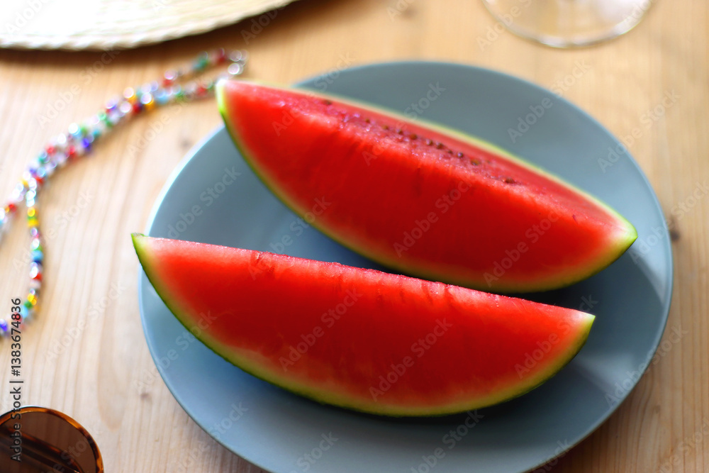 Plate with watermelon slices, glass of orange juice or cocktail, straw hat, colorful beaded necklace and sunglasses on the wooden table. Summer essentials concept. Selective focus.