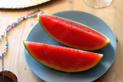 Plate with watermelon slices, glass of orange juice or cocktail, straw hat, colorful beaded necklace and sunglasses on the wooden table. Summer essentials concept. Selective focus.