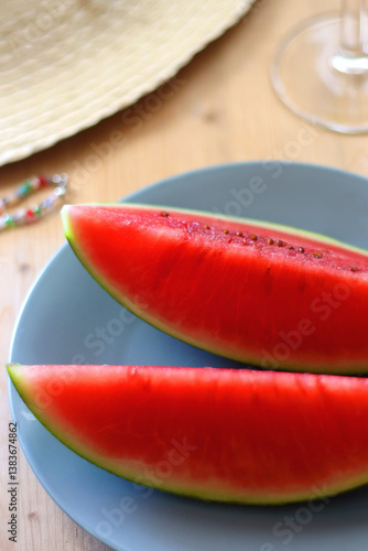 Plate with watermelon slices, glass of orange juice or cocktail, straw hat, colorful beaded necklace and sunglasses on the wooden table. Summer essentials concept. Selective focus.