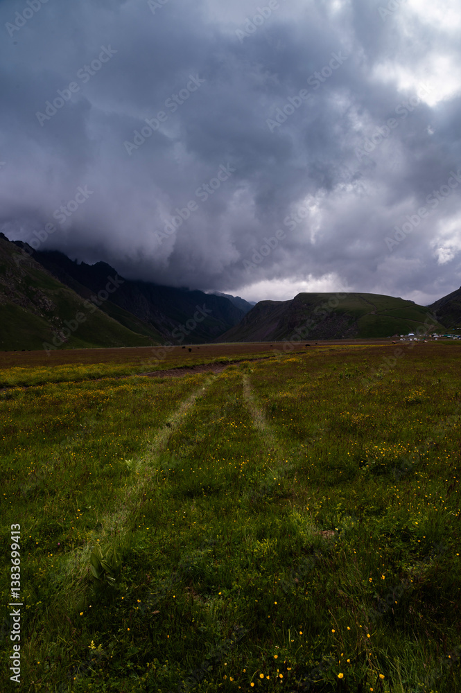 Obraz premium Off-road adventure through fields into the mountains. Majestic mountains tower in the background, lush greenery at your feet and ever-changing weather, storm clouds
