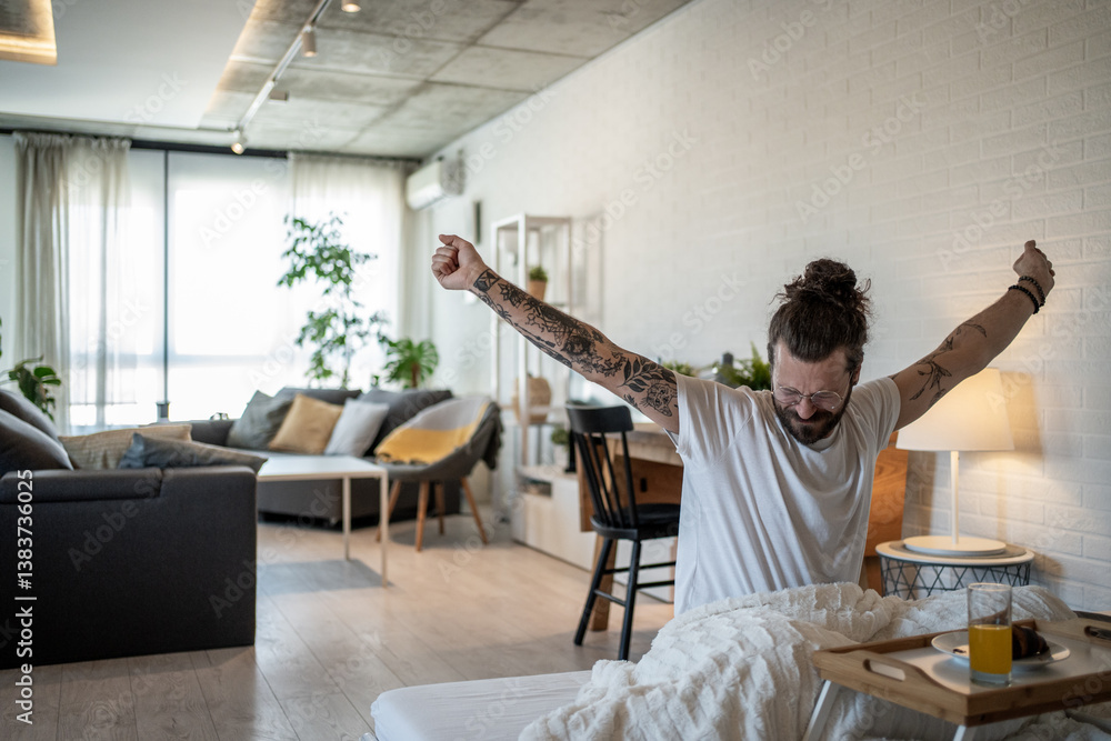 Fototapeta premium Tattooed freelancer waking up and stretching in bed at home