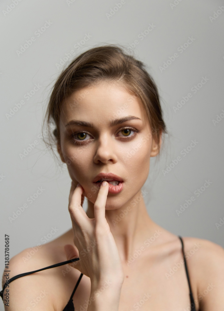 Young woman with a thoughtful expression, gently touching her lips, wearing a simple black top. Soft gray background enhances her striking features. Young woman with a thoughtful expression, gently touching her lips, wearing a simple black top. Soft gray background enhances her striking features.