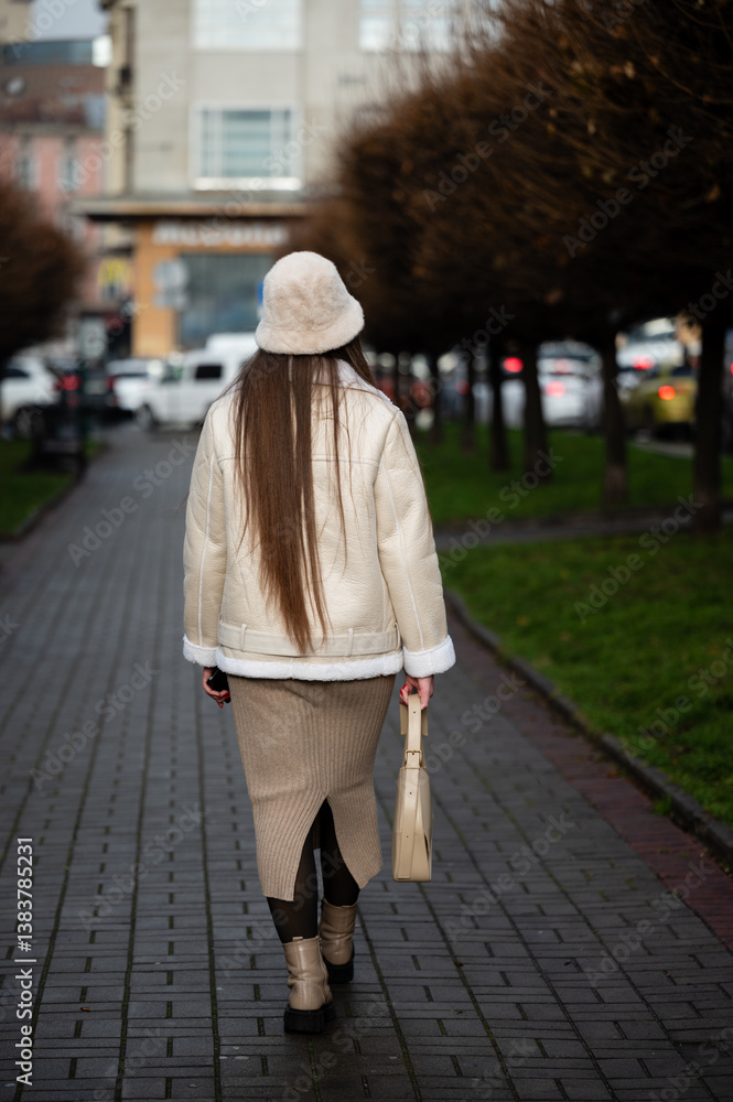 Elegant stroll through a tree-lined pathway as a woman embraces the charm of the city in cool weather, radiating style and grace during a late afternoon in autumn