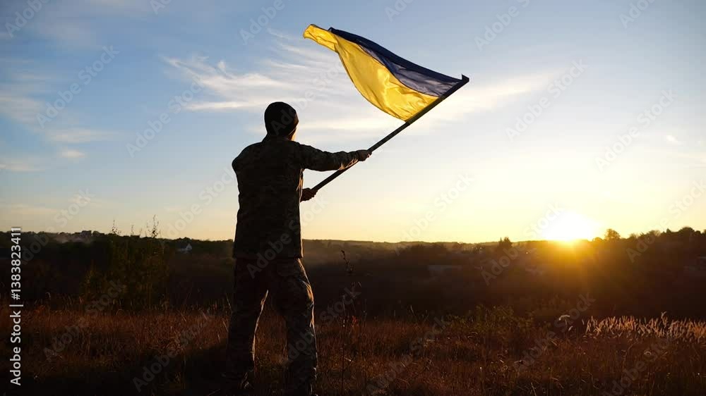 Ukrainian army man waving national banner against background of sunset. Young male soldier lifted flag at countryside. Victory against russian aggression. End of war between russia and Ukraine