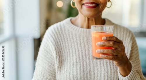 Elderly african female smiling holding healthy juice in cozy sweater indoors