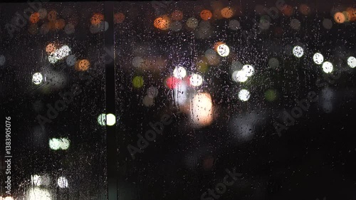 Horizontal video of defocused lights on the background and rain drops on the foreground at night.